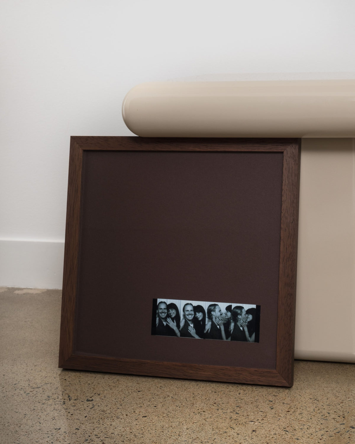 Bare in Walnut with chocolate mat and a photo-booth strip placed low on the mat, leaning on the floor