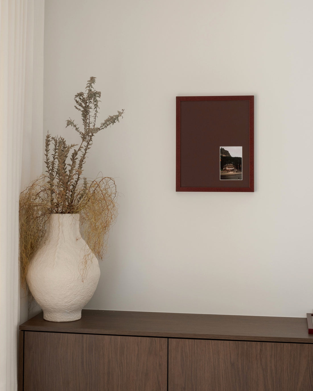 Bias in Merlot hung above a walnut cabinet beside a white vase