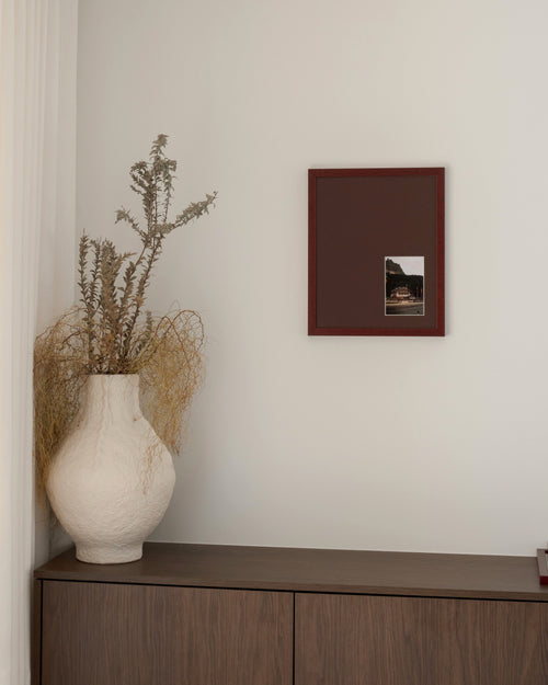 Bias in Merlot hung above a walnut cabinet beside a white vase