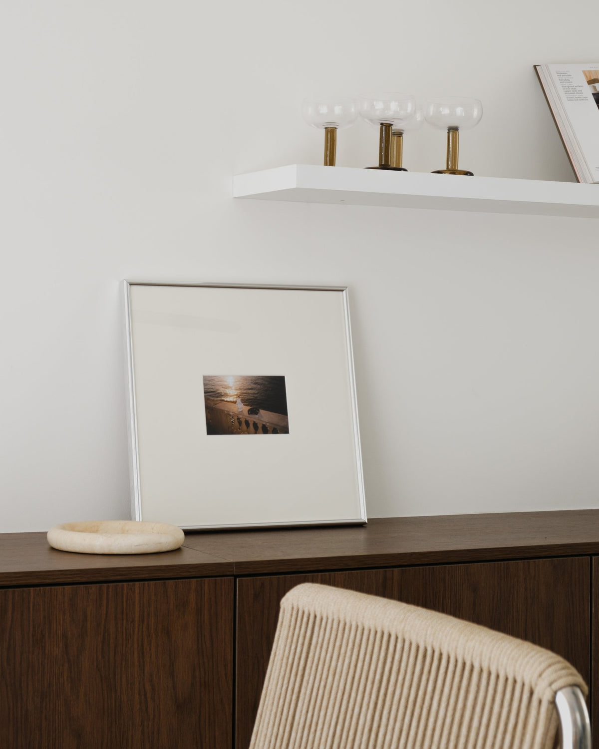 Still in Chrome with ivory mat, leaning on a walnut cabinet