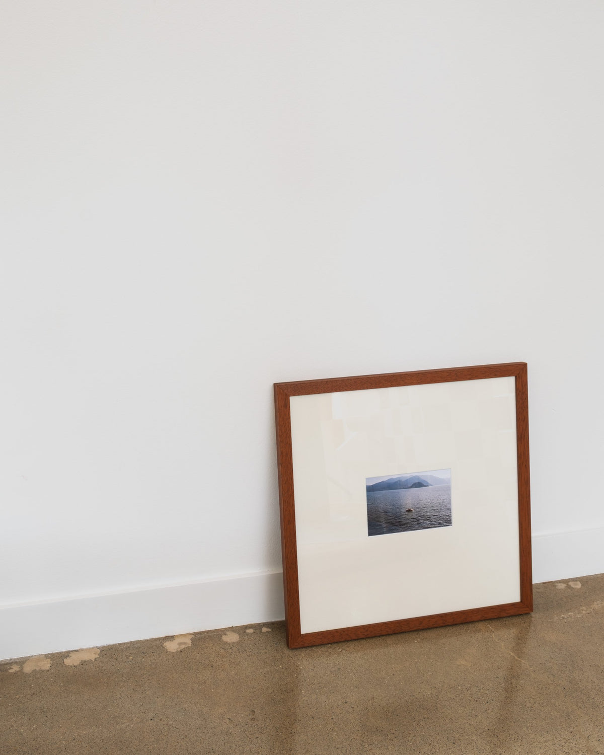Still in Teak with ivory mat and a lake photo, leaning against a white wall on a concrete floor