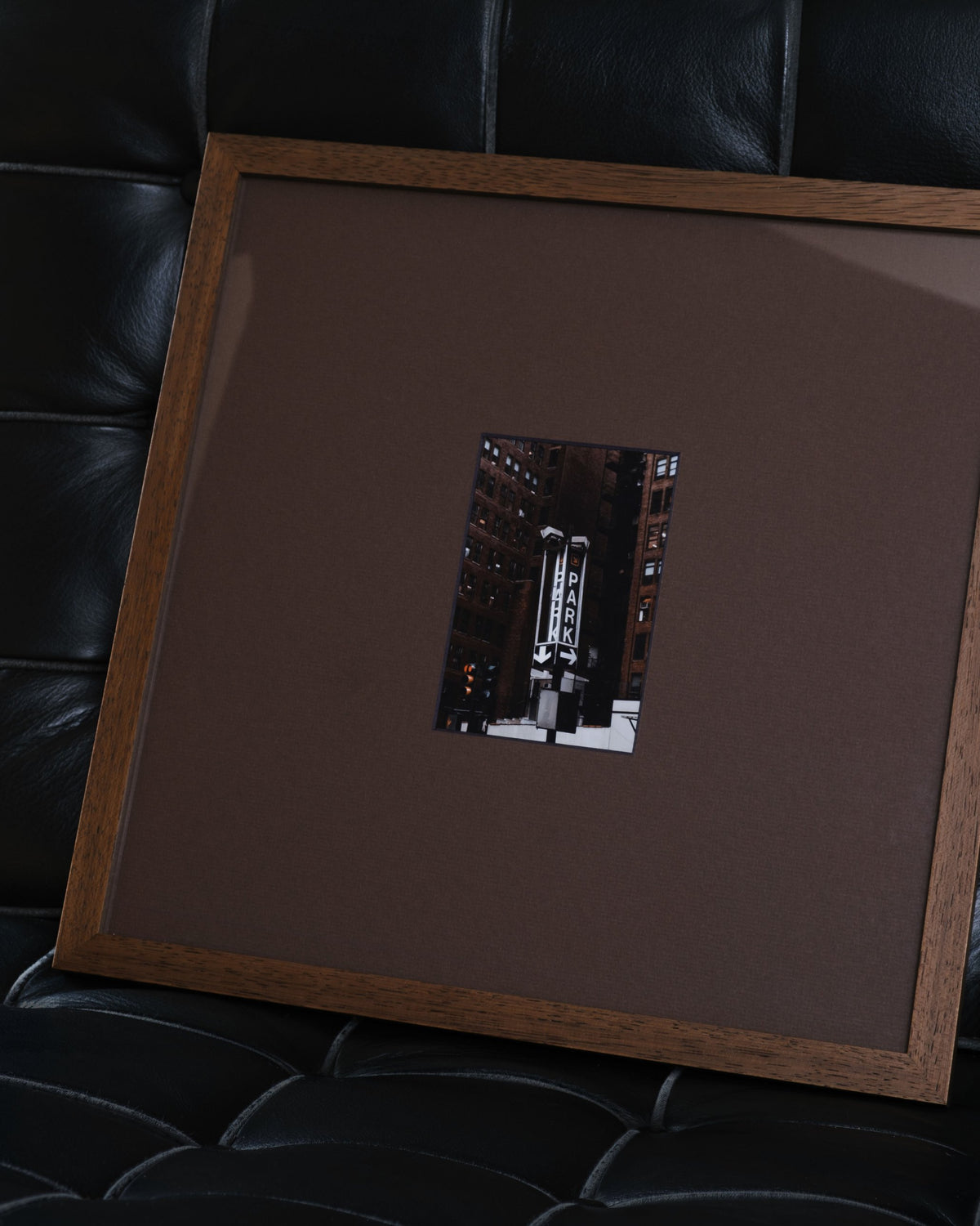 Still in Walnut with chocolate mat, a city street photo in the cutout, leaning on a black leather chair